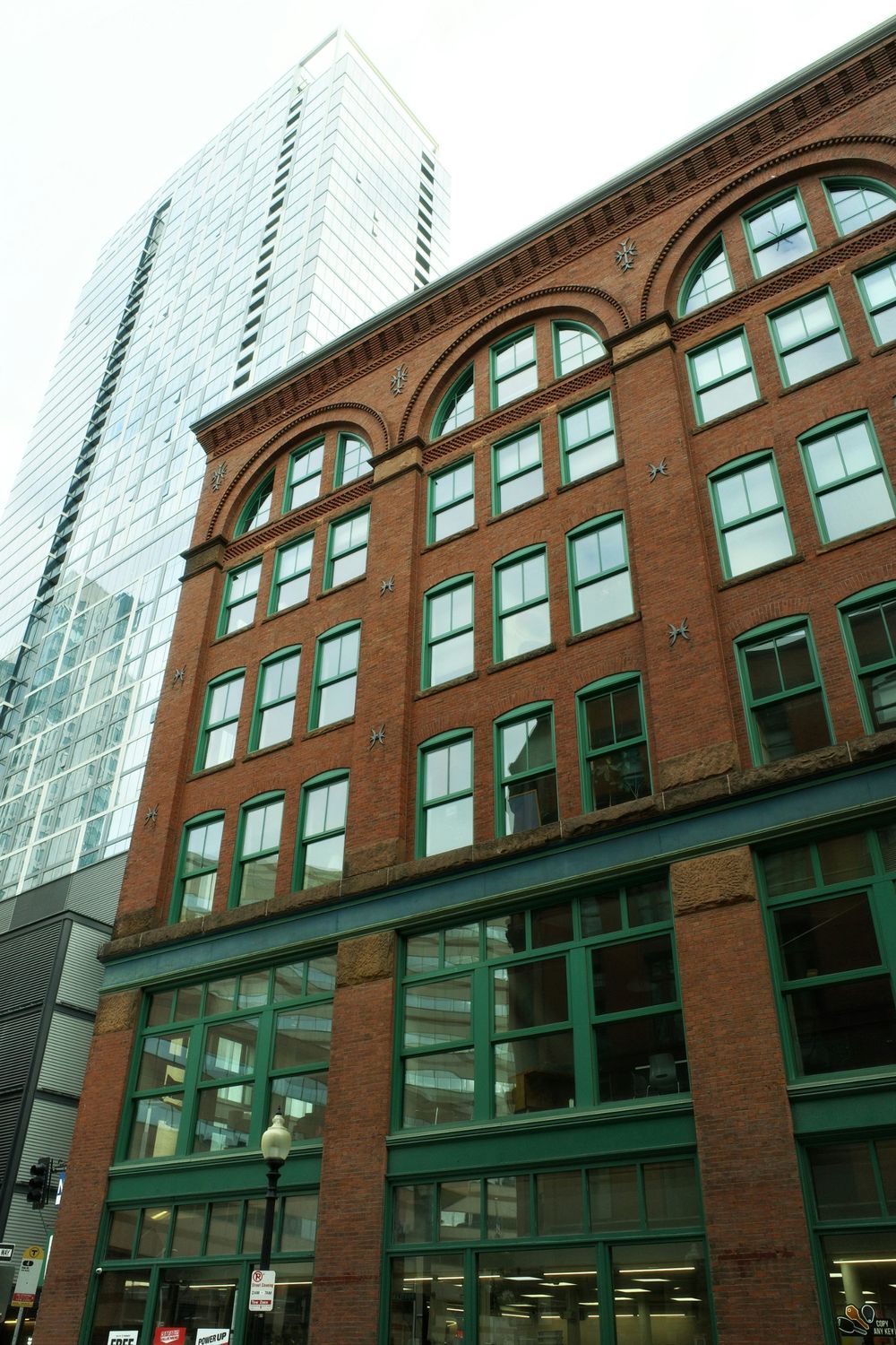 Brick commercial building with green-framed windows in front of a glass office tower